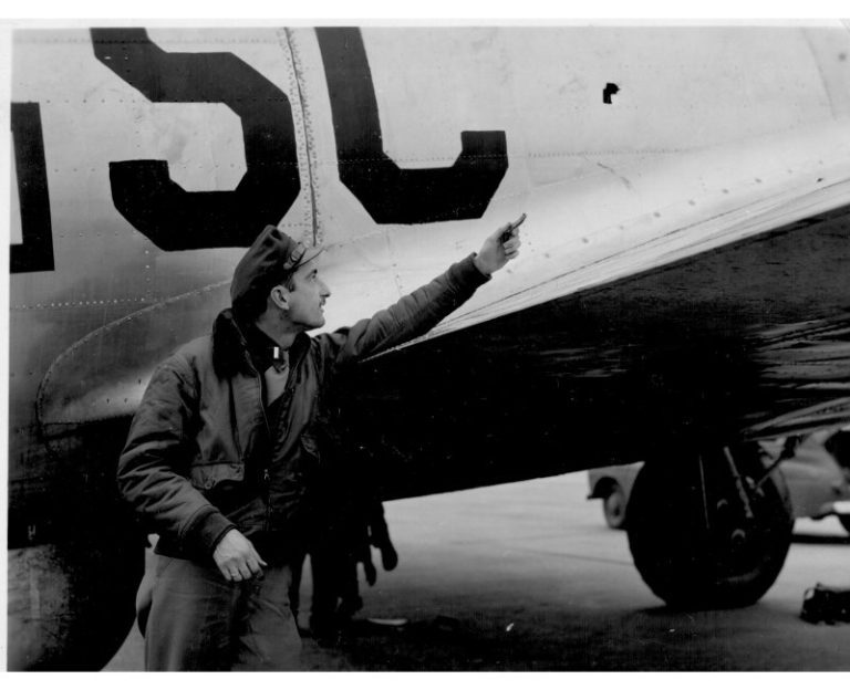 Close call. Lieutenant Stan Fine points a shard of flak at the hole through which it burse, narrowly missing his arm but damaging his radar equipment while on a bomb run over Ludwigshaven